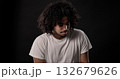 Young african-american man with curly hair looking down and thinking against black background 132679626