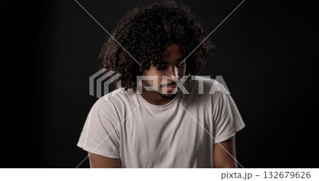 Young african-american man with curly hair looking down and thinking against black background 132679626
