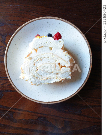Slice of meringue roulade on a plate with berries on a wooden table Slice of meringue roulade on a plate with berries on a wooden table 132680423