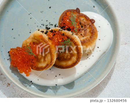 Pancakes served with red caviar. Delicious pancakes on sour cream on blue plate decorated natural red caviar of fish. Close up. Top view or flat lay 132680456