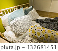 Cozy bedroom interior with colorful pillows and patterned bedding on an unmade bed. Modern home design with playful polka dots and bright yellow accents creating a cheerful, relaxed atmosphere. 132681451