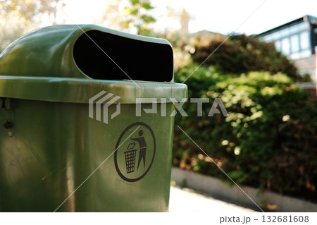 Detailed close-up view of green trash bin with waste icon, located in park area under sunlight. Clean environment and eco-friendly concept Detailed close-up view of green trash bin with waste icon, located in park area under sunlight. Clean environment and eco-friendly concept 132681608