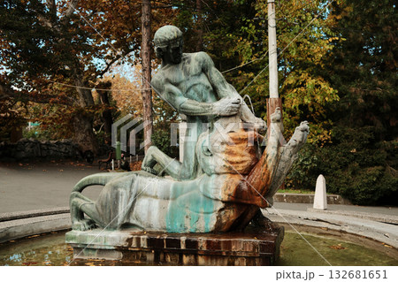 Bronze statue of a man fighting a lion at the fountain in Belgrade Zoo surrounded by autumn trees. Historic and artistic detail 132681651