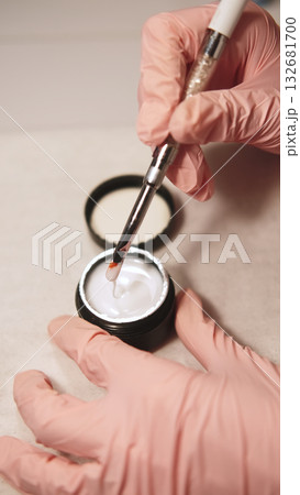 Gel nail procedure. Acrylic salon treatment. Female beautician hands in pink protective gloves holding brush over fluid polish open bottle. Gel nail procedure. Acrylic salon treatment. Female beautician hands in pink protective gloves holding brush over fluid polish open bottle. 132681700
