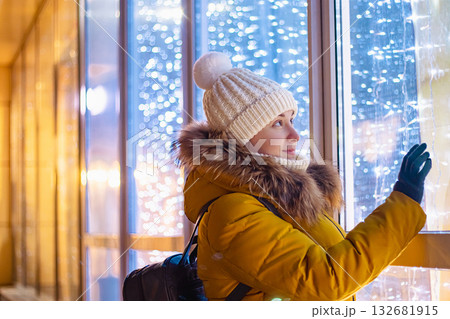 Young woman in winter clothes looks at shiny store window. Christmas shopping and sales. 132681915