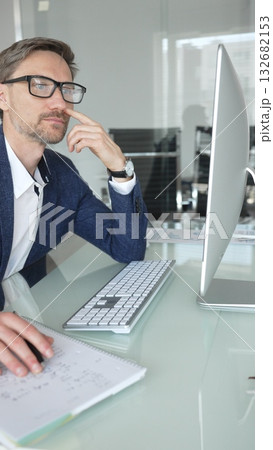 Businessman in a blue jacket thinking and brainstorming ideas while working on computer and taking notes in modern office. Business people concept Businessman in a blue jacket thinking and brainstorming ideas while working on computer and taking notes in modern office. Business people concept 132682153