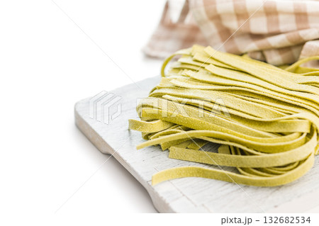 Green tagliatelle pasta on cutting board isolated on white background. Green tagliatelle pasta on cutting board isolated on white background. 132682534