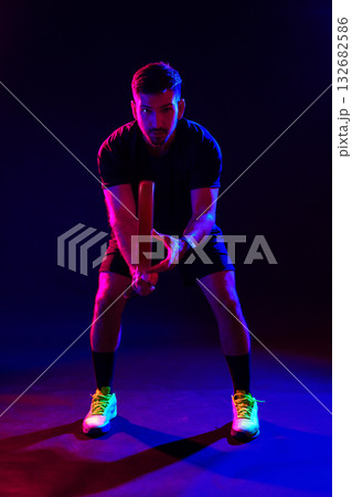 Man prepares to swing a bat in a colorful neon-lit sports environment Man prepares to swing a bat in a colorful neon-lit sports environment 132682586