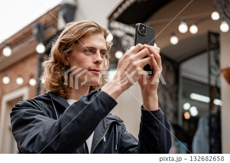 Young man takes a photo while standing outside a store on a cloudy day Young man takes a photo while standing outside a store on a cloudy day 132682658