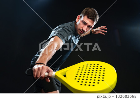 Man swings a yellow paddle racket during an intense indoor sports session Man swings a yellow paddle racket during an intense indoor sports session 132682668