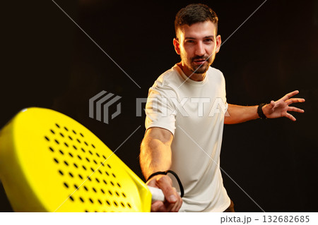 Man practicing padel with a bright yellow racket in a dark studio 132682685