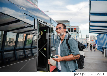 Handsome man boarding bus, holding sport ball and phone. 132682711