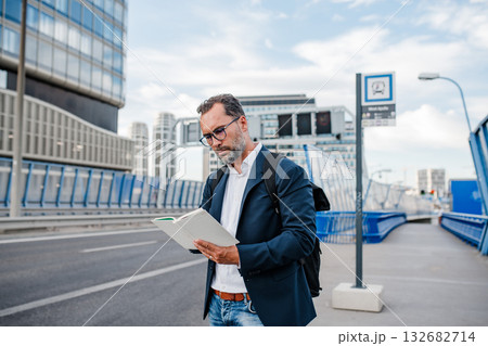 Mature man reading while waiting for bus. Mature man reading while waiting for bus. 132682714