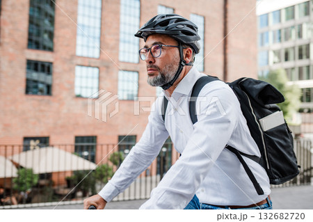 Man riding bike to work in city with helmet and backpack 132682720