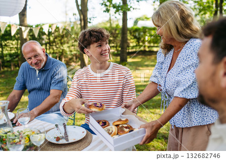 Senior woman serving grilled food during family grill party. 132682746