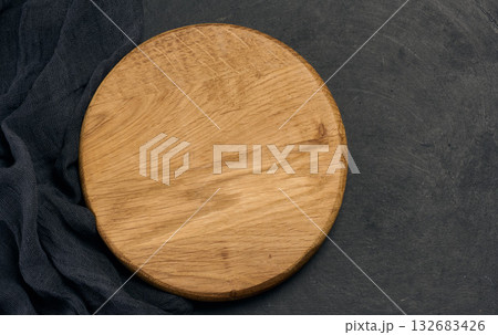 Empty round brown wooden cutting board on a black background 132683426
