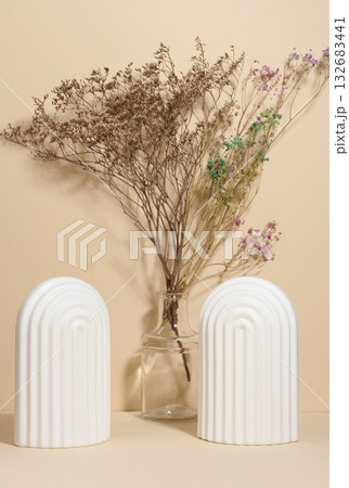 A vase with dried flowers and two white fluted arches on a beige background 132683441