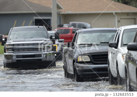 Flooded Florida road with evacuating cars and surrounded with water houses in suburban residential area. Consequences of hurricane natural disaster 132683553