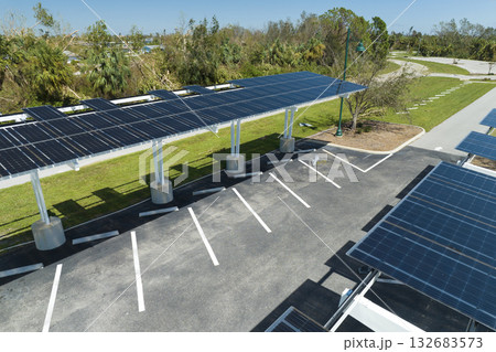 Failing of photovoltaic technology integrated in urban infrastructure. Hurricane wind damage to solar panels installed as shade roof over parking lot for parked electric cars 132683573