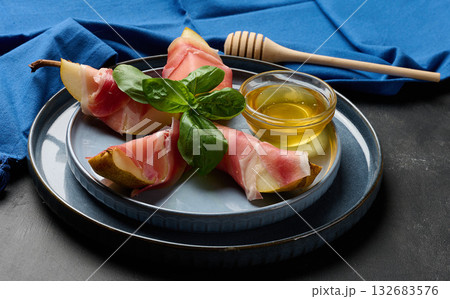 Gourmet appetizer of pear wrapped in prosciutto on a blue ceramic plate. Gourmet appetizer of pear wrapped in prosciutto on a blue ceramic plate. 132683576