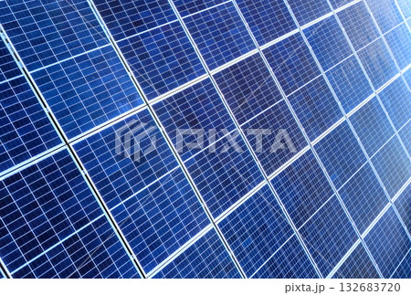 Close-up surface of lit by sun blue shiny solar photo voltaic panels. System producing renewable clean energy. Renewable ecological green energy production concept. Close-up surface of lit by sun blue shiny solar photo voltaic panels. System producing renewable clean energy. Renewable ecological green energy production concept. 132683720