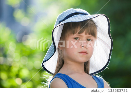 Close-up portrait of serious little girl in a big hat. Child having fun time outdoors in summer. 132683721