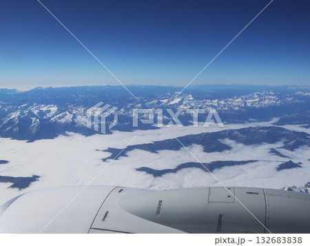 Aerial View Over Snowy Mountain Range With Clouds From An Airplane Window Aerial View Over Snowy Mountain Range With Clouds From An Airplane Window 132683838