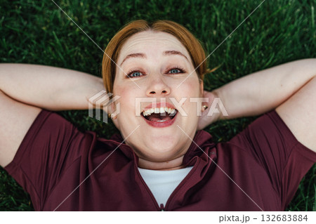 Beautiful plus size woman lying on grass after outdoors training session. 132683884