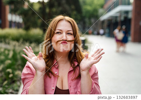 Funny portrait of mid-size woman making a hair mustache. Funny portrait of mid-size woman making a hair mustache. 132683897