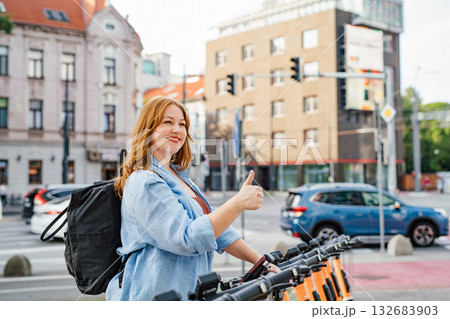 Curvy woman unlocking shared e-scooter in city. 132683903