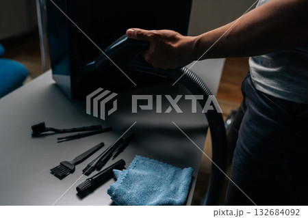 Computer technician cleaning computer case with vacuum cleaner, different brushes and microfiber cloth on table, performing maintenance and removing dust in dark workshop, close-up. 132684092
