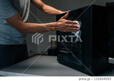 Close-up cropped shot of technician cleaning dust from computer case in dark workshop, emphasizing importance of maintenance for optimal performance and hygiene. Concept of service, cleaning PC. 132684093