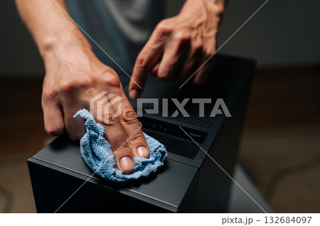 Close-up of technician hands cleaning computer case with blue microfiber cloth, ensuring dust and debris removed for optimal performance in dark workshop. Concept of service, cleaning desktop PC. Close-up of technician hands cleaning computer case with blue microfiber cloth, ensuring dust and debris removed for optimal performance in dark workshop. Concept of service, cleaning desktop PC. 132684097
