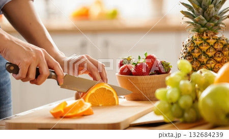 Woman hands slicing fresh orange on cutting board with fruits Woman hands slicing fresh orange on cutting board with fruits 132684239