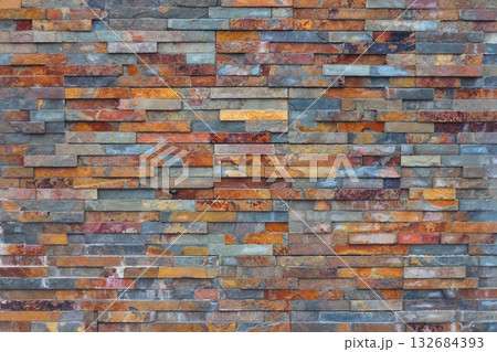 A striking wall of natural stacked slate tiles features a vibrant pattern of earthy orange, grey, and brown hues. Concept of natural stone textures, rugged beauty, and architectural finishes. A striking wall of natural stacked slate tiles features a vibrant pattern of earthy orange, grey, and brown hues. Concept of natural stone textures, rugged beauty, and architectural finishes. 132684393