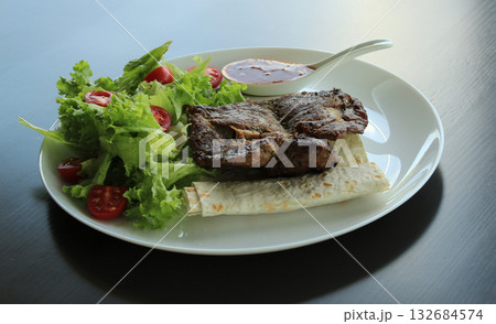 Serving of meat steak with sauce and fresh lettuce in a plate on black surface 132684574