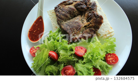 Grilled meat served with greens and pitta bread on white plate at the restaurant  132684575