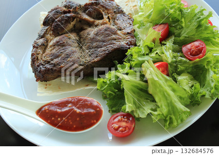 Fried meat and spicy sauce served on plate with lettuce leaves and thin bread 132684576