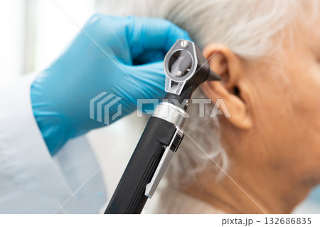 Audiologist or ENT doctor use otoscope checking ear of asian senior woman patient treating hearing loss problem. 132686835