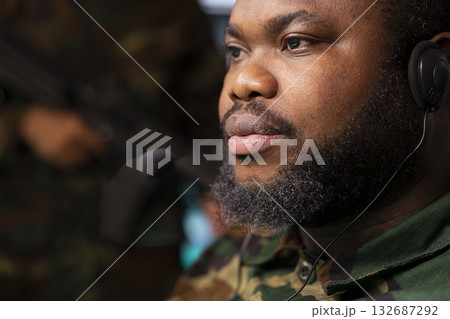 Army specialist looking at radar surveillance transmission on gear monitors, relaying data to troops using headset mic. Close up of military agent transmitting satellite tech reconnaissance info 132687292