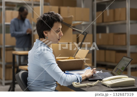 Female worker overseeing custom orders logistics and product handling, working at a fulfillment center workstation. Packing goods in the storage room of growing local shipping startup. Female worker overseeing custom orders logistics and product handling, working at a fulfillment center workstation. Packing goods in the storage room of growing local shipping startup. 132687319