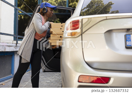 African american urban courier with massive pile of pizza boxes, delivering fast food order from a restaurant. Driving the courier service car to bring bigger meal orders, pizza delivery. 132687332