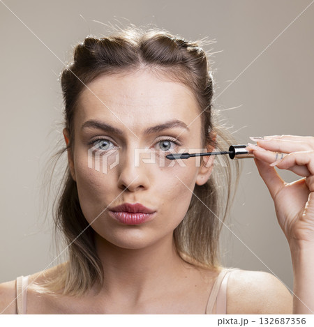 Radiant female model with minimal makeup applying mascara for thick lashes. Her glowing complexion and nude tones embodying feminine strength and natural beauty, subtle products. Radiant female model with minimal makeup applying mascara for thick lashes. Her glowing complexion and nude tones embodying feminine strength and natural beauty, subtle products. 132687356