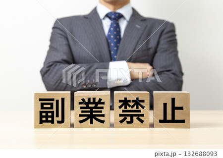 「副業禁止」と書かれたブロックと腕組みをするビジネスマン 132688093