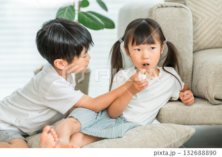 リビングのソファーでおやつを食べる仲良しの兄妹 リビングのソファーでおやつを食べる仲良しの兄妹 132688890