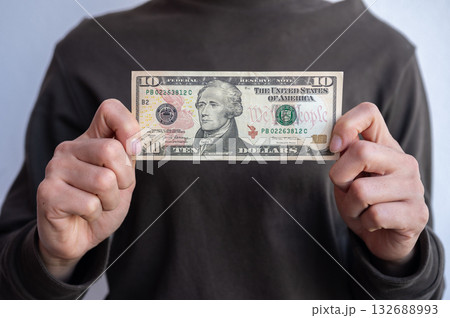 Cropped shot view of woman holding and showing ten American dollar banknotes in hands. The US Dollar is the currency of United States. Cropped shot view of woman holding and showing ten American dollar banknotes in hands. The US Dollar is the currency of United States. 132688993