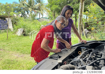 Women look under the hood of a broken car to find engine problems 132690390