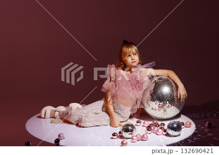 Studio portrait of young girl in festive outfit with disco balls on burgundy background 132690421