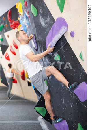Male climber ascending colorful holds on indoor bouldering wall 132690509