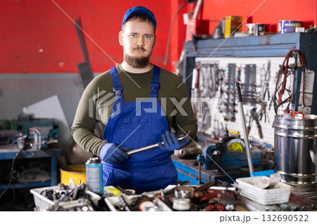 Positive male worker of car workshop holding metal tool in car workshop 132690522